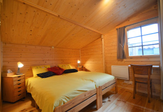 Chambre en bois au Chalet de Bioul en Belgique, lit double jaune, deux tables de chevet, bureau et fenêtre.