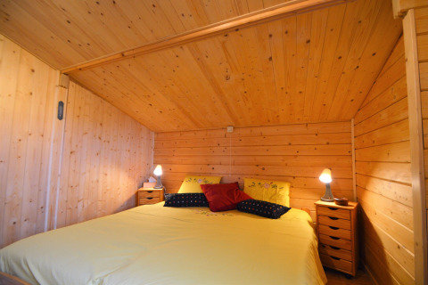 Chambre chaleureuse en bois, grand lit et tables de nuit au chalet Le Chalet de Bioul, en Belgique.