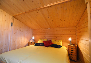 Chambre chaleureuse en bois, grand lit et tables de nuit au chalet Le Chalet de Bioul, en Belgique.