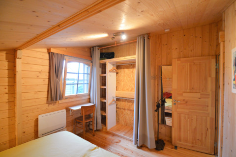 Chambre lambrissée avec placard ouvert, bureau et chaise au Chalet de Bioul en Belgique.