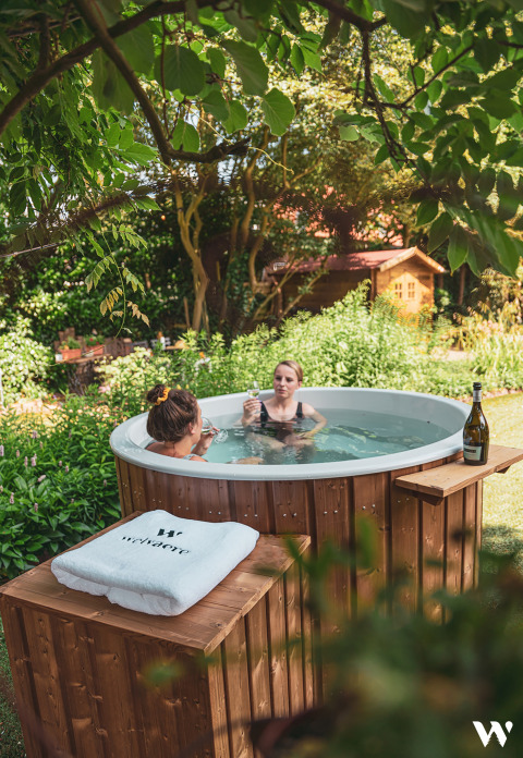 Twee vrouwen ontspannen in een ronde houten hottub, omgeven door groen, bij Soof Retreats Utrecht.