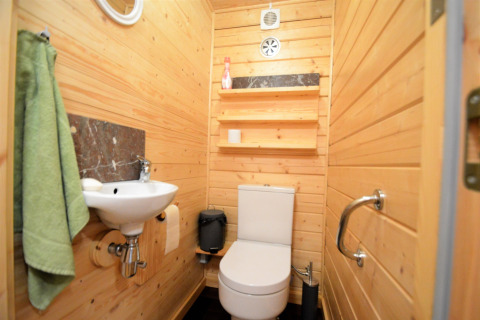 Petite salle de bain avec panneaux en bois, lavabo, toilettes blanches, étagères et serviette verte.