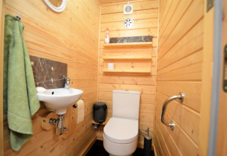 Petite salle de bain avec panneaux en bois, lavabo, toilettes blanches, étagères et serviette verte.