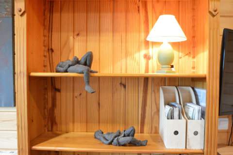Étagère en bois avec lampe, deux sculptures de personnages allongés et range-documents au Chalet de Bioul.