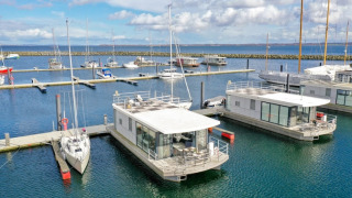 Houseboat moderne e barche a vela sono ormeggiate in un porto turistico sotto un cielo blu nuvoloso.