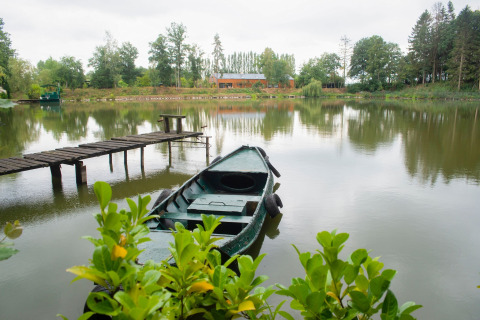 Rustig beeld van een boot bij de oever van Le Bateau du Lac Privé in België, met huis en bomen op de achtergrond.