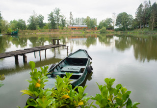 Rustig beeld van een boot bij de oever van Le Bateau du Lac Privé in België, met huis en bomen op de achtergrond.