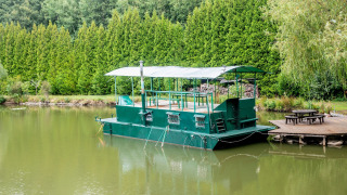 Groen woonboot Le Bateau du Lac Privé aangemeerd aan een rustige vijver met houten picknickterras.