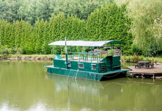 Groen woonboot Le Bateau du Lac Privé aangemeerd aan een rustige vijver met houten picknickterras.