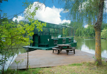 Houseboat 'Le Bateau du Lac Privé' ormeggiato su un lago privato con terrazza e tavolo da picnic in Belgio.