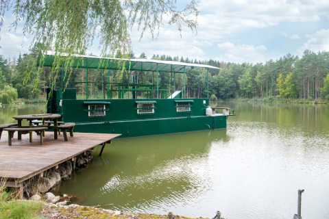 Groen woonboot aangemeerd aan een rustige steiger op een meer, omgeven door bos bij Le Bateau du Lac Privé, België.
