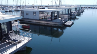 Moderne woonboten aangemeerd in een rustige haven, omringd door zeilboten en helder, weerspiegelend water.