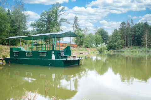 Het woonboot 'Le Bateau du Lac Privé' drijft rustig op een Belgisch meer, omringd door groene bomen.