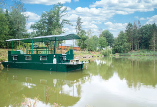 Het woonboot 'Le Bateau du Lac Privé' drijft rustig op een Belgisch meer, omringd door groene bomen.