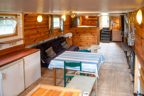 Interieur van woonboot 'Le Bateau du Lac Privé' in België met houten wanden, bank en eettafel.