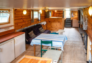 Interieur van woonboot 'Le Bateau du Lac Privé' in België met houten wanden, bank en eettafel.