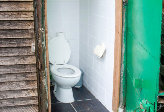 Bagno esterno su una houseboat in Belgio, piastrelle bianche, porta in legno e telaio metallico verde.
