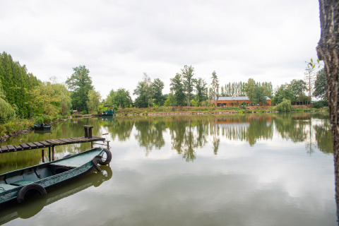 Hus på søbredden med båd ved kajen og træer, set ved Le Bateau du Lac Privé i Belgien.