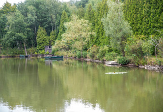 Rustig meer met dichtbegroeide bomen en een boot bij «Le Bateau du Lac Privé» in België.