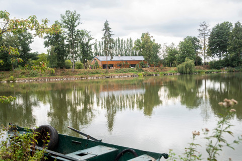 Woonboot aan een privémeer in België, groene boot op de voorgrond, bomen weerspiegeld in het water.