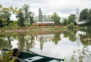 Woonboot aan een privémeer in België, groene boot op de voorgrond, bomen weerspiegeld in het water.