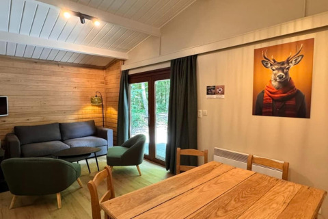 Vista interior del chalet 'OREE DU BOIS' en Bélgica, sala de estar acogedora y cuadro de un ciervo con bufanda.
