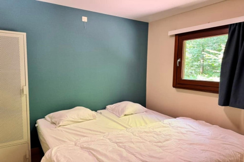 Slaapkamer in chalet OREE DU BOIS in België met twee bedden, groene muur, raam en witte kast.