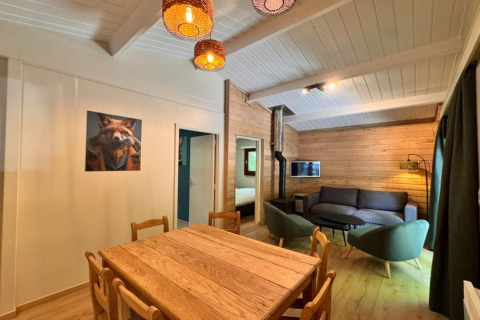 Interior del chalet OREE DU BOIS en Bélgica, con paredes de madera, mesa de comedor y área de estar acogedora.