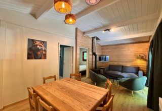 Interior del chalet OREE DU BOIS en Bélgica, con paredes de madera, mesa de comedor y área de estar acogedora.
