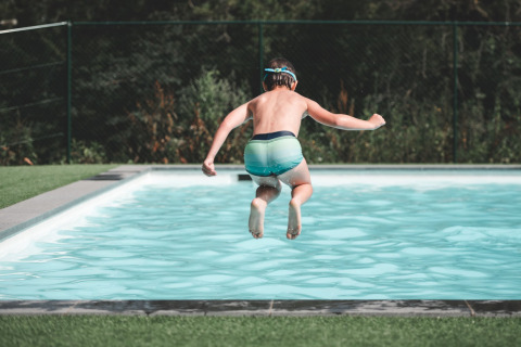 Een kind springt in het zwembad bij Holiday Park Ardinam 1 in België, omgeven door natuur.