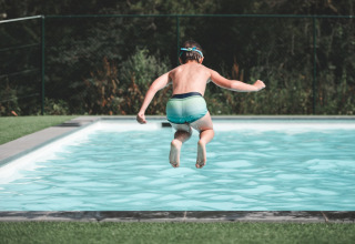A child jumps into a swimming pool at Holiday Park Ardinam 1 in Belgium, surrounded by green nature.