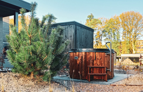 Houten hottub naast een modern vakantiehuis en groene dennenstruik bij Soof Retreats in Utrecht, Nederland.