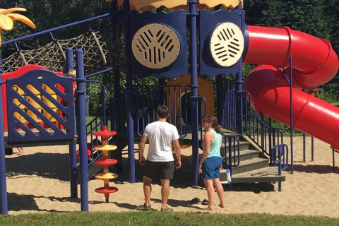 Due adulti vicino a un colorato parco giochi con scivolo al Holiday Park Ardinam 1 in Belgio.