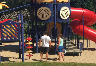 Due adulti vicino a un colorato parco giochi con scivolo al Holiday Park Ardinam 1 in Belgio.