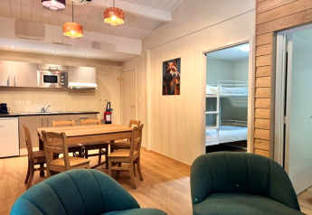 Interieur van chalet OREE DU BOIS in België met eettafel, keuken en stapelbedden op de achtergrond.