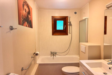 Baño color beige en el chalet OREE DU BOIS en Bélgica, con bañera, ventana y cuadro de erizo en la pared.