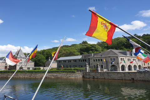 Diverse bandiere europee sventolano sopra un fiume al Holiday Park Ardinam 1 in Belgio con cielo sereno.