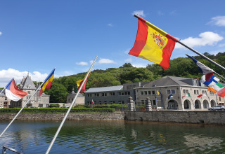 Meerdere Europese vlaggen wapperen boven de rivier bij Holiday Park Ardinam 1 in België onder blauwe lucht.
