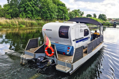 Foto van de Watercamper Deluxe houseboot met caravan op het water in Duitsland, omgeven door natuur.