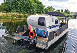 Foto van de Watercamper Deluxe houseboot met caravan op het water in Duitsland, omgeven door natuur.