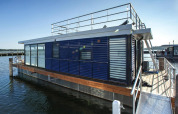 Casa flotante moderna 'Floating Houses Blue Active' atracada en Ribnitz-Damgarten, Alemania, día soleado.