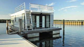 Modernes Hausboot namens Floating House 'Leni' liegt in Ribnitz-Damgarten an einem sonnigen Steg vor Anker.