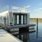 Moderne woonboot genaamd Floating House 'Leni' aangemeerd in Ribnitz-Damgarten bij een steiger onder blauwe lucht.