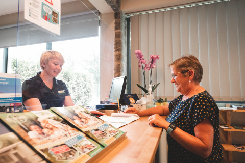 Twee vrouwen praten bij de receptie van Holiday Park Ardinam 1 in België met folders op de balie.