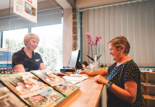 Twee vrouwen praten bij de receptie van Holiday Park Ardinam 1 in België met folders op de balie.
