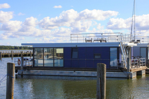 Casa flotante moderna llamada 'Luisa' atracada en Ribnitz-Damgarten, con amplios ventanales y terraza.