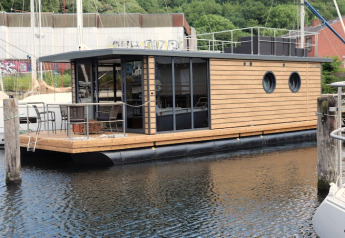 Een modern woonboot genaamd Houseboat Leni ligt aangemeerd in de haven met terras en zitgedeelte.