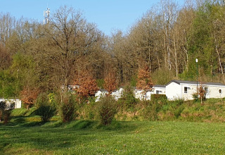 Mobile homes at Holiday Park Ardinam 1 in Belgium, nestled by forest and greenery under a clear blue sky.