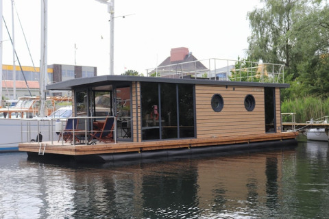 Modern houseboat named Houseboat Lina with wood paneling, docked at a harbor in Germany.