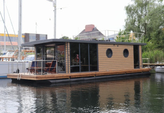 Modern houseboat named Houseboat Lina with wood paneling, docked at a harbor in Germany.